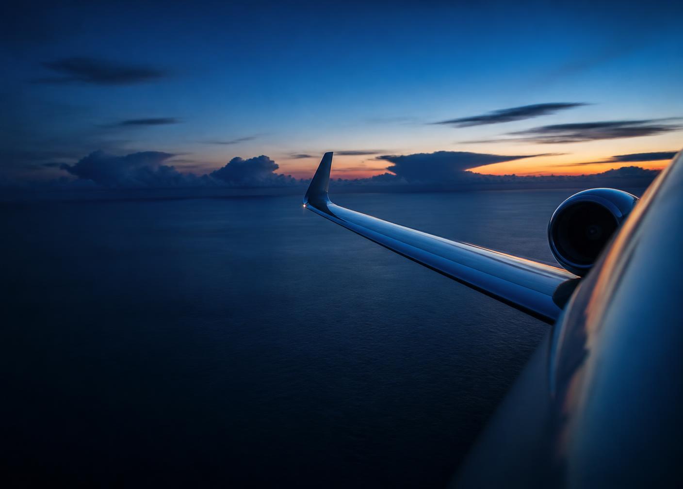 Private jet wing above a dark ocean at dusk